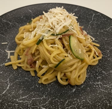 A plate of creamy linguine pasta carbonara with zucchini and grated parmesan cheese.