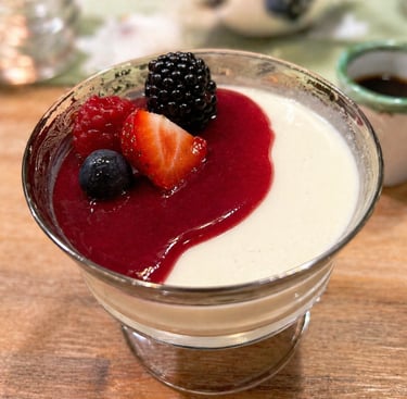 Creamy vanilla panna cotta dessert topped with red berry coulis and fresh mixed berries in a glass bowl.
