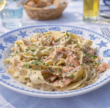 Creamy salmon tagliatelle pasta served on a blue nautical plate at an outdoor seaside table.