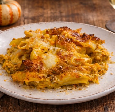 Baked pumpkin pasta casserole with melted cheese on a plate with fall decor and white wine.