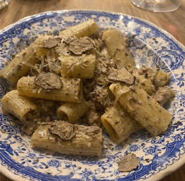 Rigatoni pasta with creamy truffle sauce and fresh black truffle shavings on a blue floral plate.
