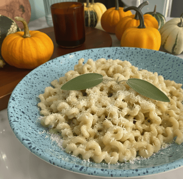 Creamy pumpkin pasta with parmesan cheese and fresh sage leaves on a blue speckled plate.
