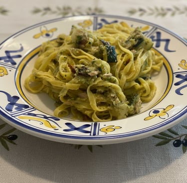 Fresh fettuccine pasta with zucchini, tuna, and pesto sauce served on an ornate Italian ceramic plate.