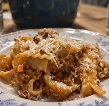Traditional mafaldine pasta with savory bolognese meat sauce and grated parmesan cheese on a vintage floral plate.