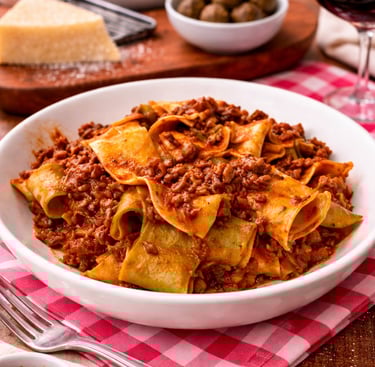 Pappardelle pasta with hearty beef bolognese sauce served in a white bowl on a red checkered napkin.