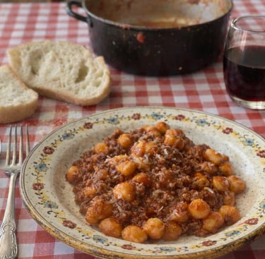 Homemade potato gnocchi with savory meat bolognese sauce served with red wine and crusty bread.