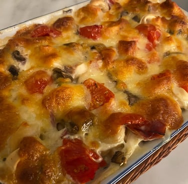 Baked pasta casserole with melted bubbly golden cheese, fresh cherry tomatoes, and mushrooms in a ceramic dish.