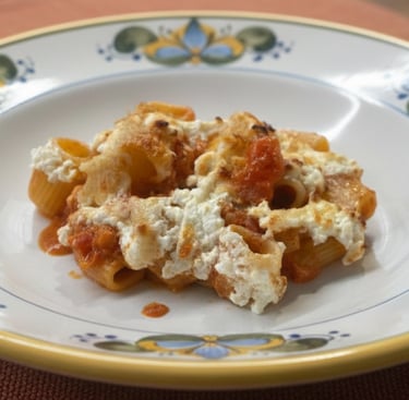 Baked rigatoni pasta with tomato sauce and melted ricotta cheese on a decorative Italian ceramic plate.