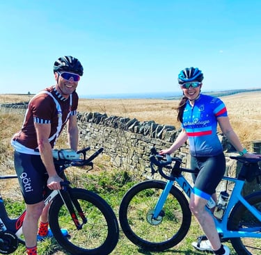 Two smiling road cyclists in gear posing with their bikes on a scenic countryside route.
