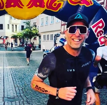 James Oswald Coaching, Doug Jones Smiling male triathlete running through a Red Bull arch during.