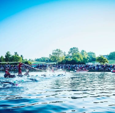 Triathletes swimming in a lake at the start of Challenge Roth with spectators on the shore.