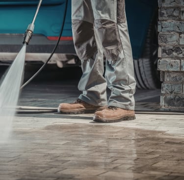 Professional worker using a high-pressure washer to clean a stone paver driveway.