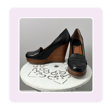 Pair of black leather platform wedge loafers for women displayed on a white decorative stool.