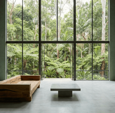 Modern minimalist living room with floor-to-ceiling windows overlooking a lush tropical forest.