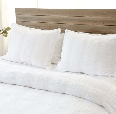 a bed with white linens quilt and pillows on top of a wooden headboard