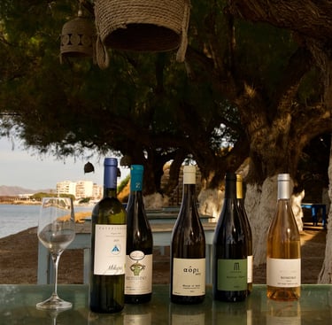 a table with greek wine bottles and wine glasses near the sea