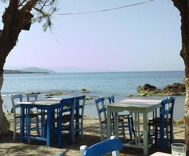 a table with chairs and tables in front of a tree near the sea