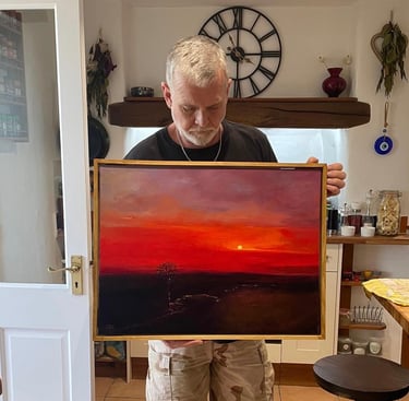 The artist holds a vibrant red sunset oil painting on canvas in a gold frame.