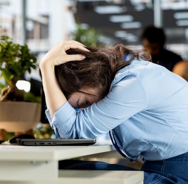 Stressed office worker resting head on desk, illustrating workplace burnout and mental health struggles.