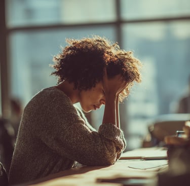 femme empathe assise à son bureau et qui se tient la tête entre les mains tellement elle est fatigué