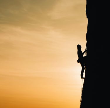 Silhouetted climber scaling steep rock face with ropes, symbolizing courage and adaptability.