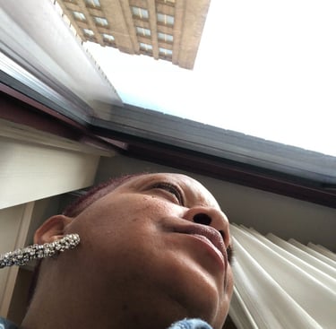 Low angle view of a woman wearing silver earrings looking out a window at a tall city building.