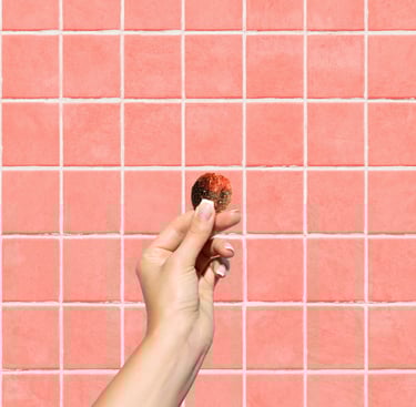 A hand holding a round piece of gummy against a pink tiled wall background.