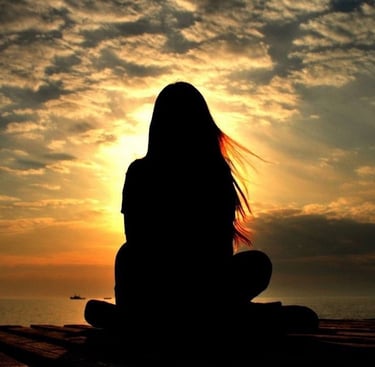 a woman sitting on a bench in front of a sunset