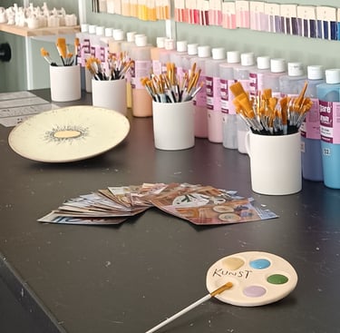 Pottery studio workbench with paintbrushes, ceramic glazes, and unpainted pottery figurines.