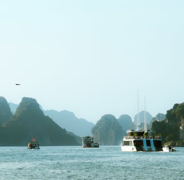 Boats sailing in Ha Long Bay, in Vietnam. In the distance are mountains and a beautiful blue sky.