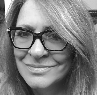 Black and white portrait of a woman with long hair wearing stylish black frame glasses.
