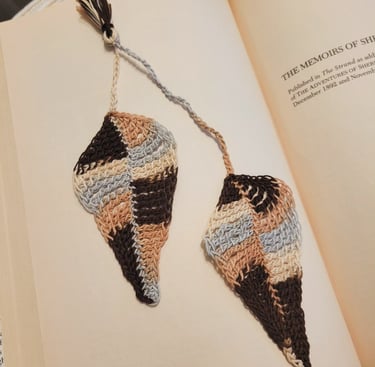 Handmade crochet leaf bookmark in neutral brown and beige tones resting inside an open book.