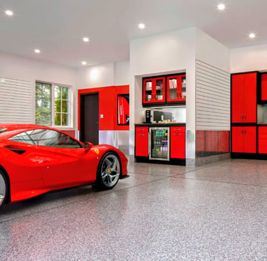 Luxury garage with a red Ferrari, epoxy flooring, and custom red storage cabinets.