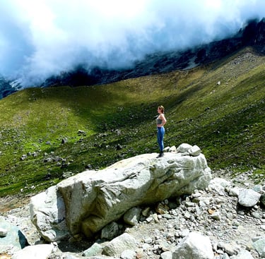 Female hiker standing on a large boulder overlooking misty green mountain peaks while trekking.