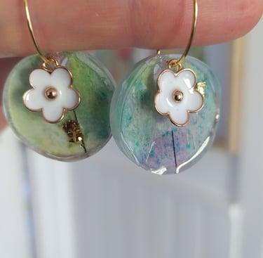 a person holding a pair of earrings with flowers