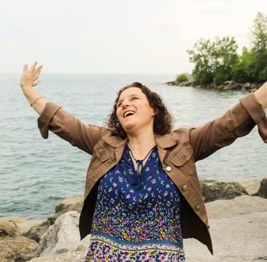 Natanya celebrating with hands in the air, lake behind