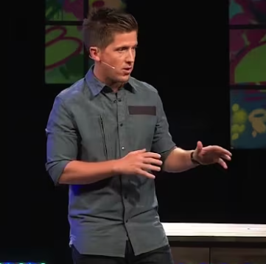 a man standing on a stage speaking to a crowd