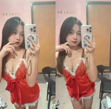 A young woman taking a mirror selfie wearing a red lace holiday-themed lingerie set with white fur trim.