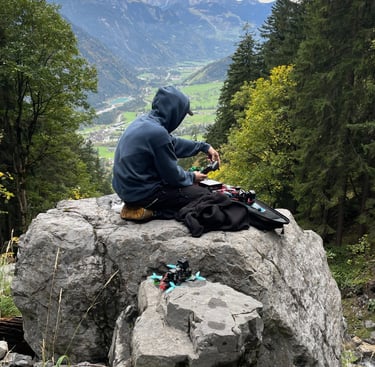 a man sitting on a rock with a backpack building up his drone setup with crossfire and googles