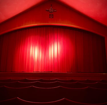A view of a stage with red curtains drawn and two spotlight illuminating them. 