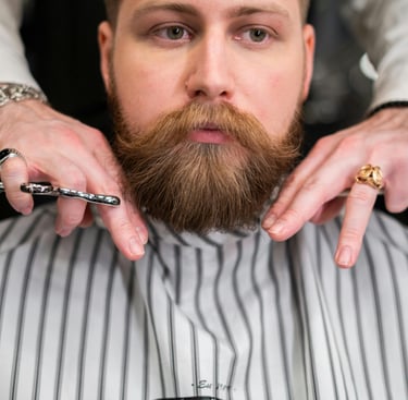 Barbero profesional recortando la barba roja y abundante de un hombre con tijeras