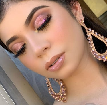 Mujer con sombra de ojos rosa con brillo y aretes colgantes llamativos con gloss labial neutro.