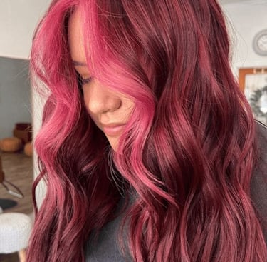 Mujer con cabello largo y ondulado con base magenta oscuro y mechones frontales