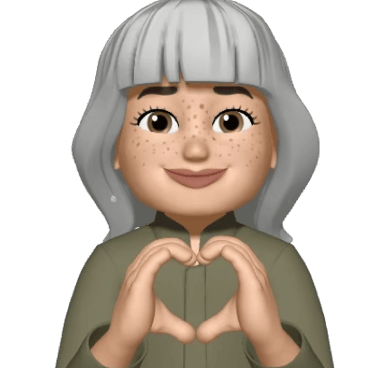 Female Memoji with grey hair and freckles making a heart shape with her hands.