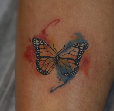 Butterfly tattoo with red and blue watercolor fill on leg by Dudo’s Hyderabad