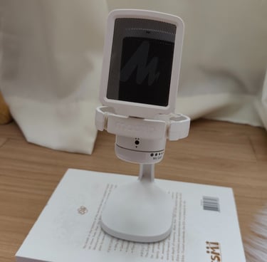 White Maono microphone with pop filter on a stand, placed on a book, with curtain background.