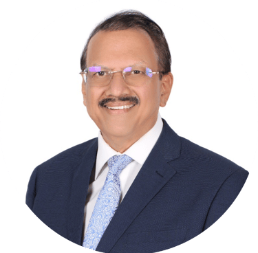 Professional portrait of a smiling Indian male executive in a blue suit and glasses against a white background.
