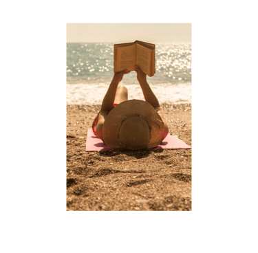 A woman on the beach lies on her back and reads a book