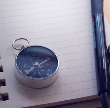 Image of compass on top of a notebook, with a pen