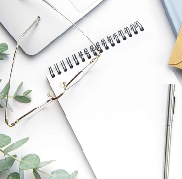 Image of a pair of glasses on top of a notepad, with a pen and a eucalyptus branch